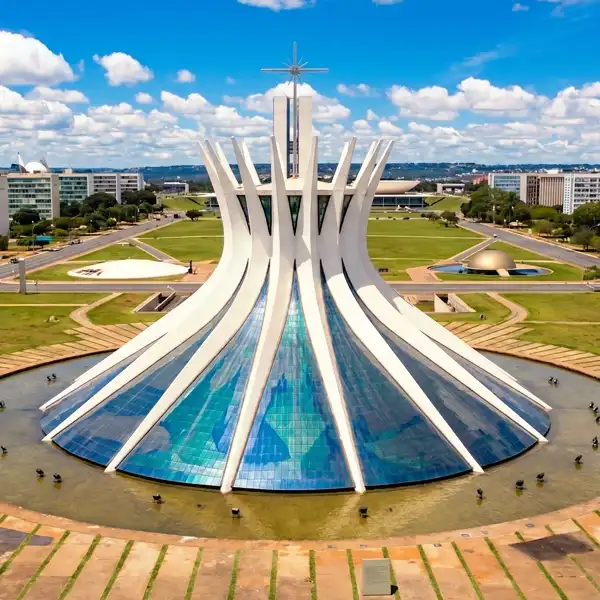 Vista aérea da Catedral de Brasília, um símbolo arquitetônico modernista e cultural localizada na capital do Brasil, com detalhes de sua estrutura única, rodeada por áreas verdes e um céu azul com nuvens brancas.