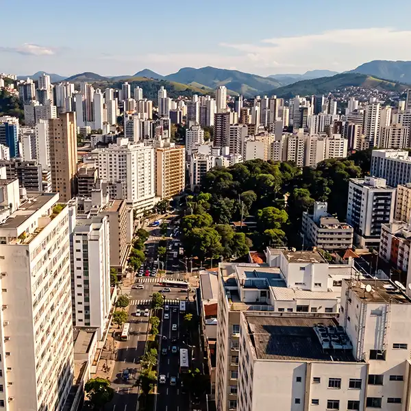 Vista panorâmica de Juiz de Fora mostrando arranha-céus, áreas verdes e montanhas ao fundo durante o dia, capturada de um ponto alto na cidade.