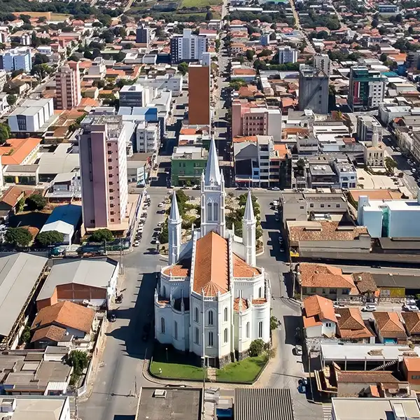Vista aérea de uma cidade com uma igreja branca de arquitetura gótica no centro, cercada por edifícios comerciais e residenciais, destacando-se na paisagem urbana.