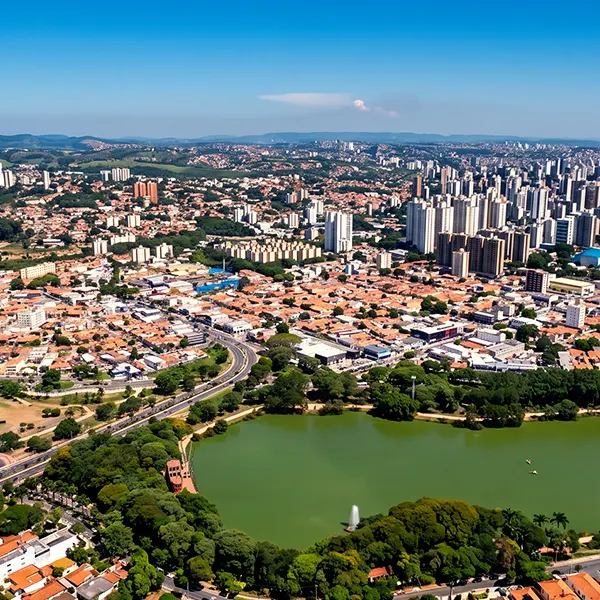 Vista aérea de uma cidade brasileira com prédios altos ao fundo, casas e avenidas em primeiro plano, e um grande lago verde cercado por vegetação, sob céu azul