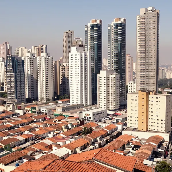 Vista panorâmica de prédios residenciais e edifícios altos em uma área urbana, com casas de telhado vermelho no primeiro plano e arranha-céus ao fundo sob céu claro.