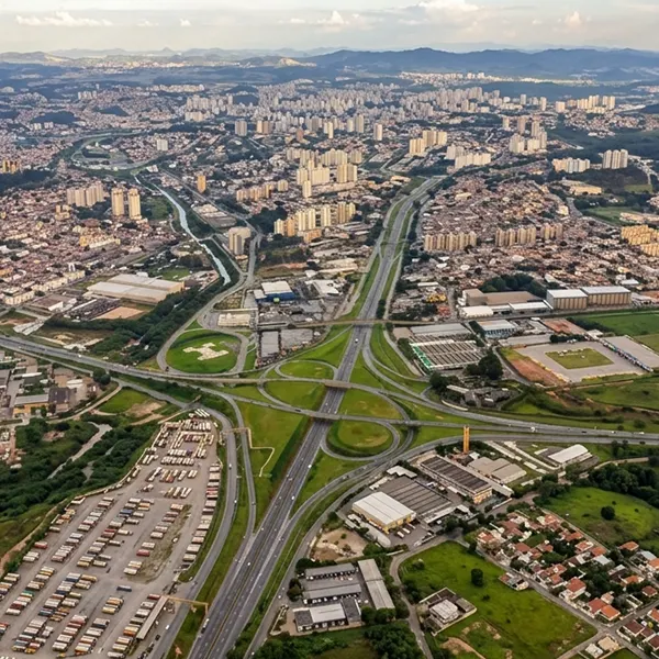 Vista aérea de uma cidade brasileira com avenidas e rodovias cruzando bairros, áreas verdes e conjuntos habitacionais ao fundo, ao entardecer.